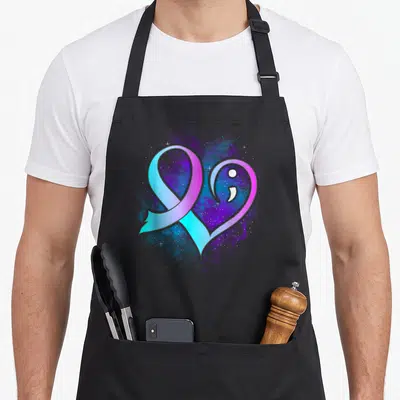 Semicolon suicide prevention apron - Gradient heart ribbon with white semicolon and stars on purple blue splatter — shown on a black cotton canvas apron against a white background