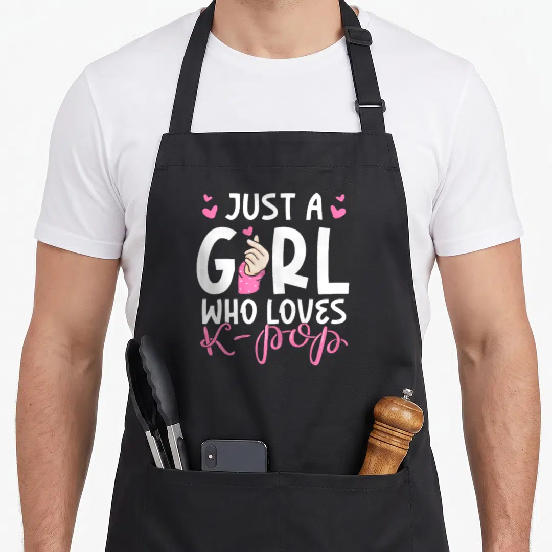 Funny k pop birthday apron - Stacked white and pink text reading Just A Girl Who Loves K-Pop with a hand making — shown on a black cotton canvas apron against a white background