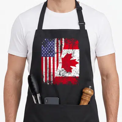 Root american flag apron - Merged distressed USA and Canada flags in red white blue on black fabric — shown on a black cotton canvas apron against a white background