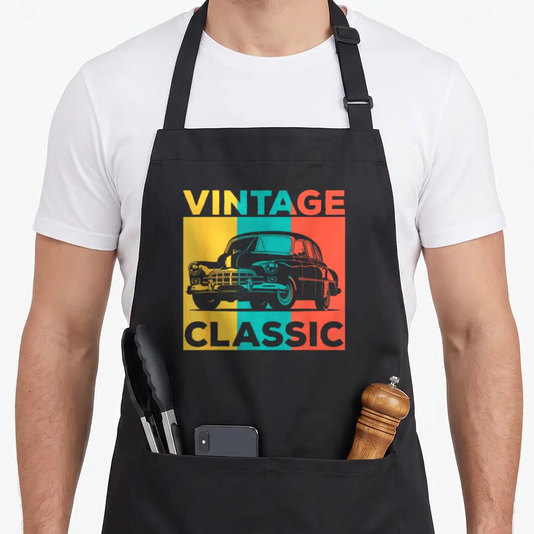 Funny enthusiast car apron - VINTAGE CLASSIC text above and below grey car on orange yellow mint green vertical stripes — shown on a black cotton canvas apron against a white background