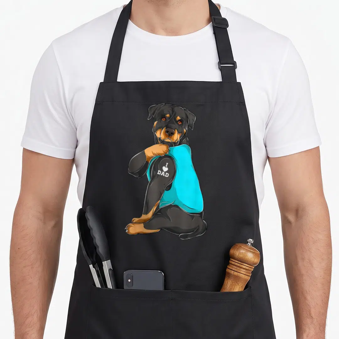 Rottweiler tattoo aprons - Cartoon rottweiler in cyan shirt showing I heart dad text on arm — shown on a black cotton canvas apron against a white background