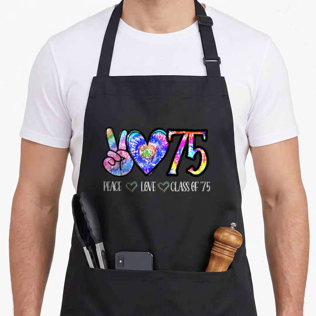 50th tie-dye apron - Tie-dye peace sign, heart, and 75 with PEACE LOVE CLASS OF '75 text — shown on a black cotton canvas apron against a white background