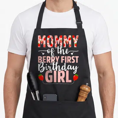 Berry birthday strawberry apron - MOMMY of the BERRY FIRST Birthday GIRL text filled with strawberries and hearts — shown on a black cotton canvas apron against a white background