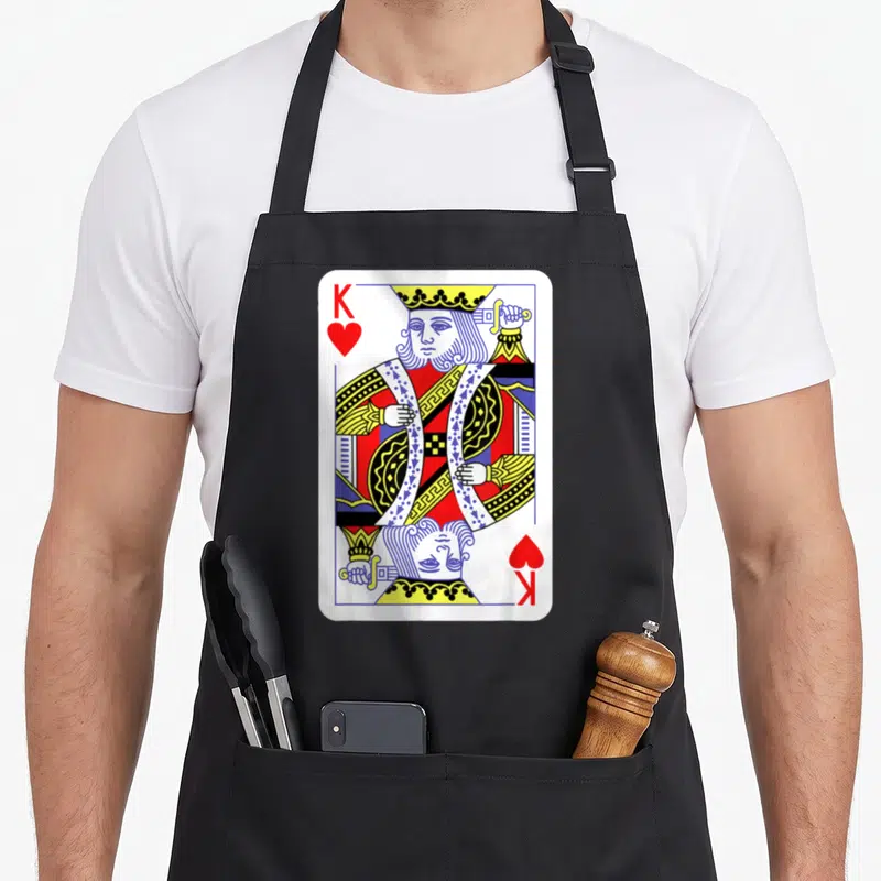 King easy apron - Mirrored King of Hearts playing card with K and heart symbols in red blue and yellow line art — shown on a black cotton canvas apron against a white background