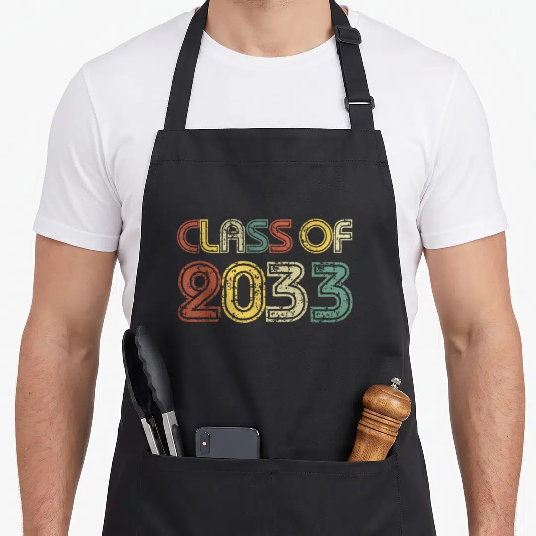 Grow graduate future class apron - Stacked CLASS OF 2033 text in orange, yellow, green, and blue vintage letters — shown on a black cotton canvas apron against a white background