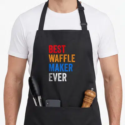 Waffle baker makers apron - Stacked text BEST WAFFLE MAKER EVER in red orange blue and white block letters — shown on a black cotton canvas apron against a white background