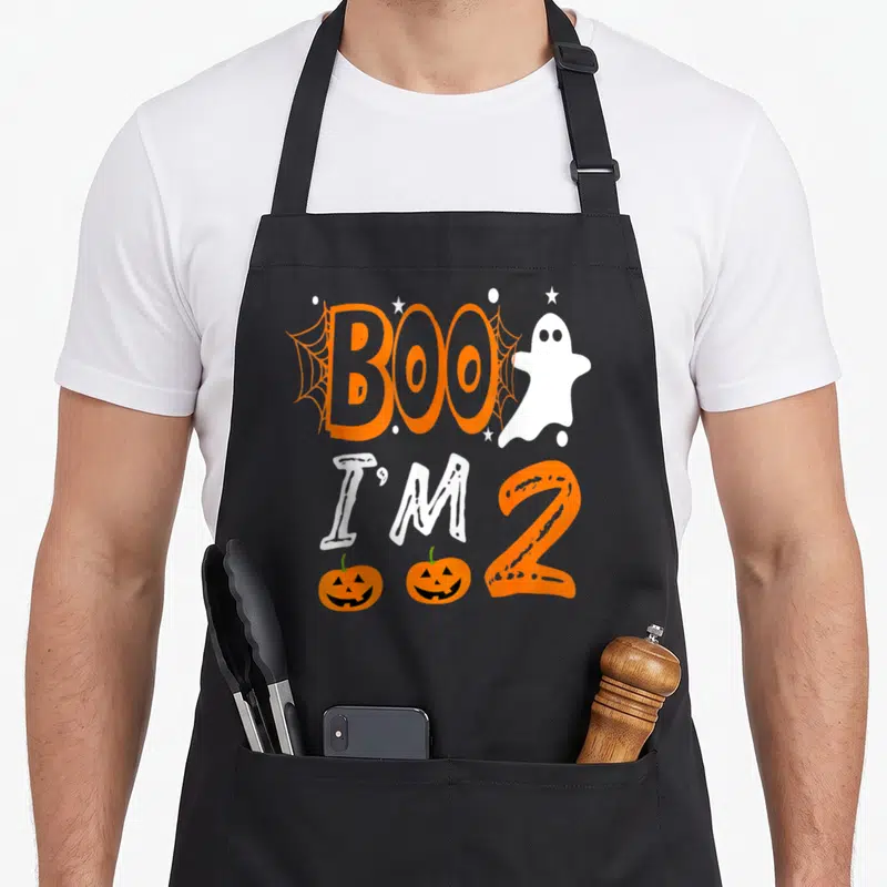 2nd funny halloween apron - Cartoon ghost and orange text reading BOO I'M 2 with two pumpkins and spider webs — shown on a black cotton canvas apron against a white background