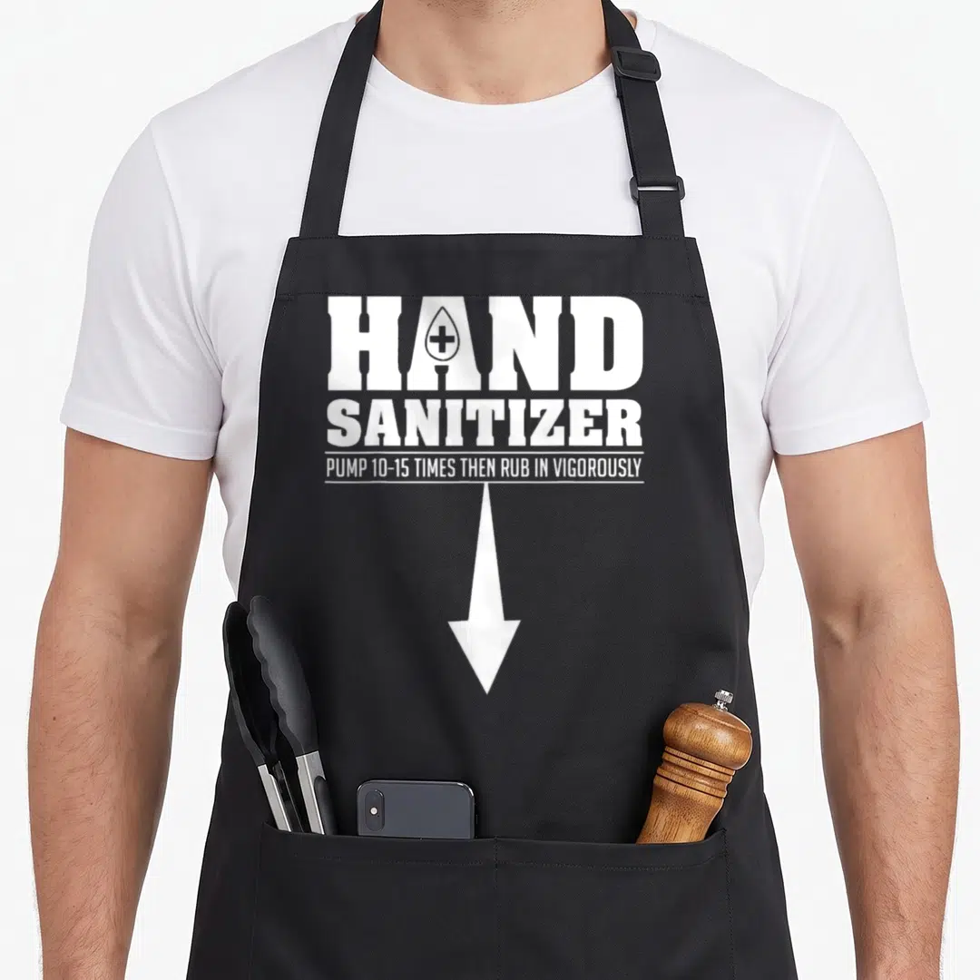 Hand the dirty apron - White text reading hand sanitizer pump 10-15 times then rub in vigorously with a downward arrow — shown on a black cotton canvas apron against a white background