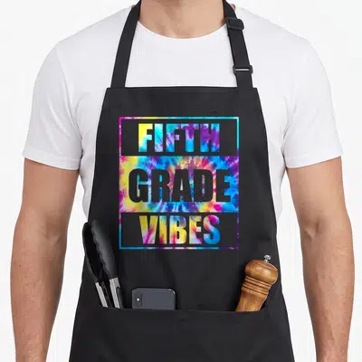 School 5th teacher apron - FIFTH GRADE VIBES tie-dye typography in grey frame with blue yellow pink purple colors — shown on a black cotton canvas apron against a white background