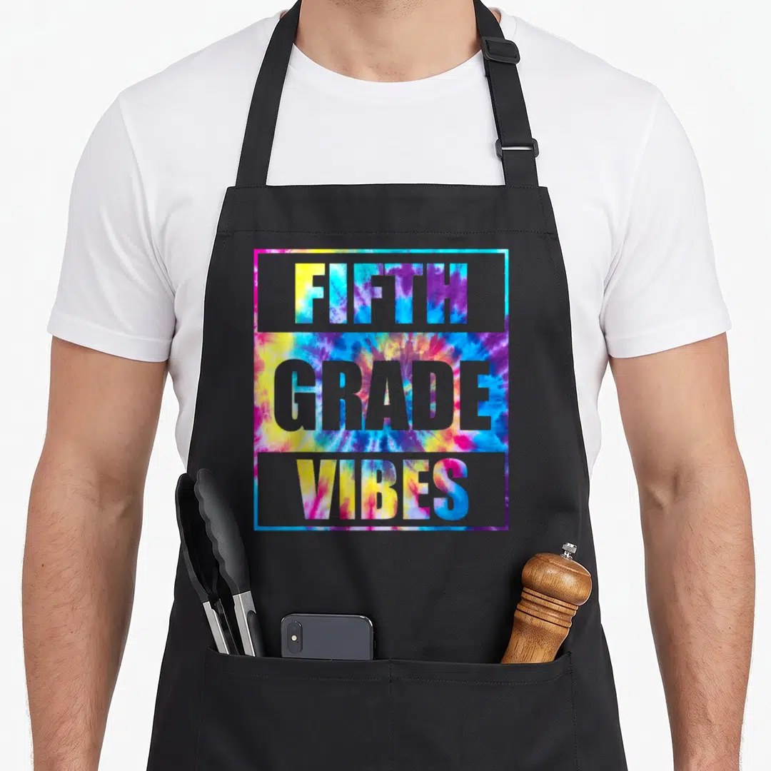 School 5th teacher apron - FIFTH GRADE VIBES tie-dye typography in grey frame with blue yellow pink purple colors — shown on a black cotton canvas apron against a white background