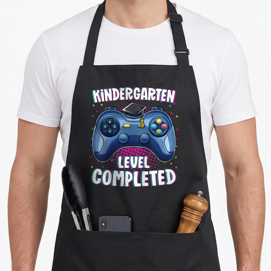 Graduation love kindergarten apron - Blue game controller wearing a graduation cap with KINDERGARTEN LEVEL COMPLETED — shown on a black cotton canvas apron against a white background