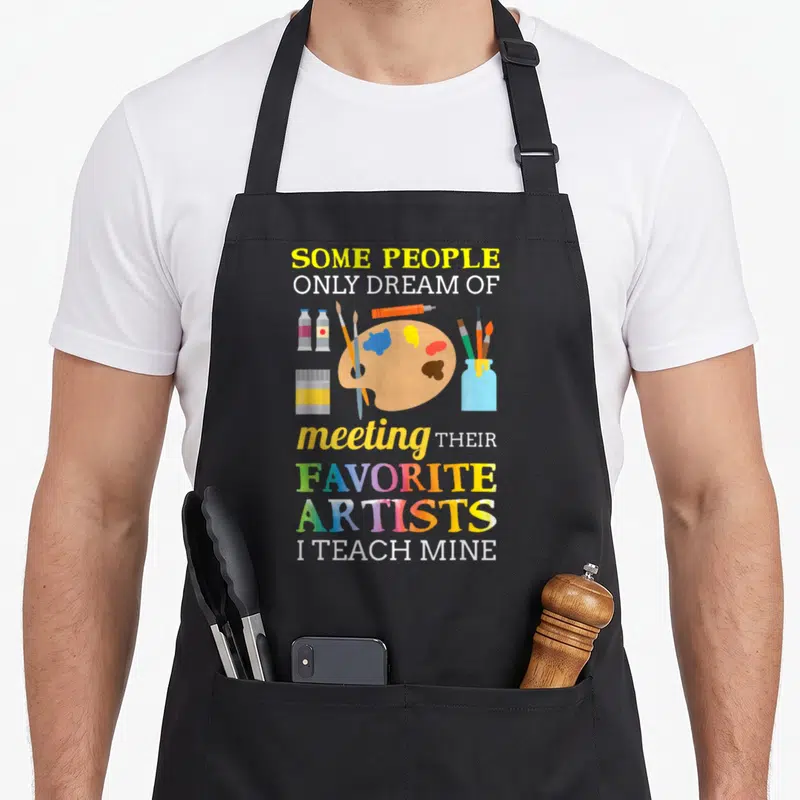 Dream teacher apron - Art supplies cluster with text Some People Only Dream Of Meeting Their Favorite Artists I Teach — shown on a black cotton canvas apron against a white background