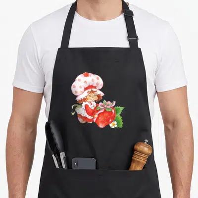 Surprise strawberry apron - Watercolor girl in strawberry hat holding giant red berry with pink bow and white flower — shown on a black cotton canvas apron against a white background