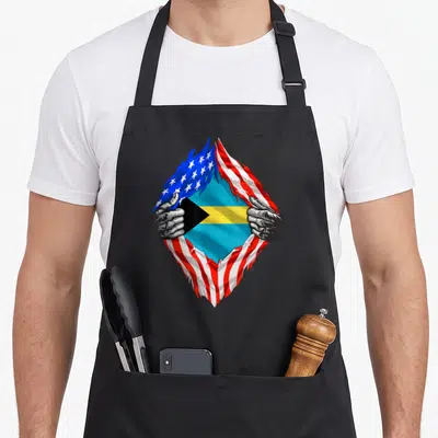 Bahamas bahamian american flag apron - Two hands tear USA flag to reveal Bahamian flag in blue red white yellow — shown on a black cotton canvas apron against a white background