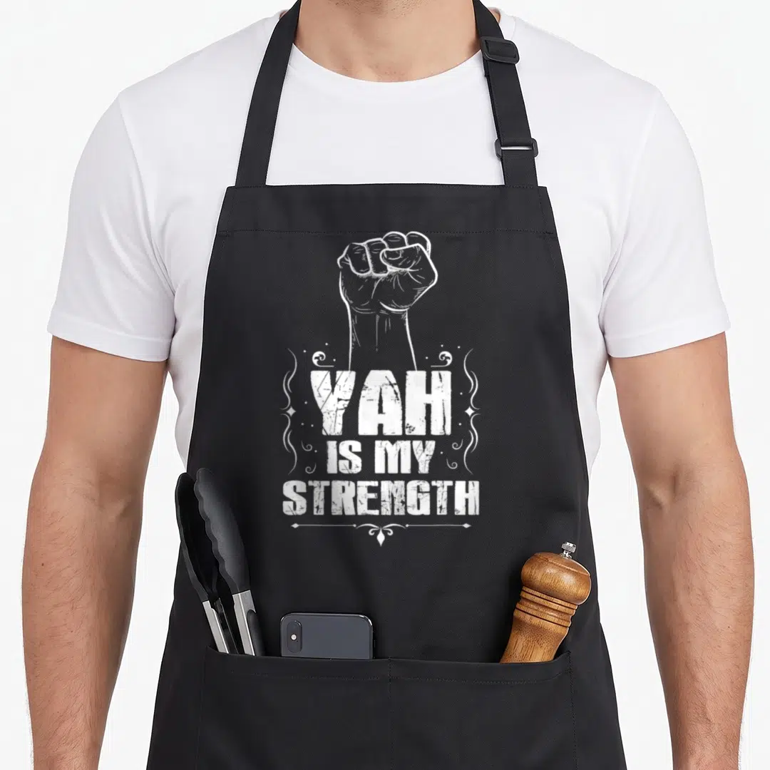 Strength hebrew aprons - White distressed clenched fist above stacked YAH IS MY STRENGTH text with swirls — shown on a black cotton canvas apron against a white background