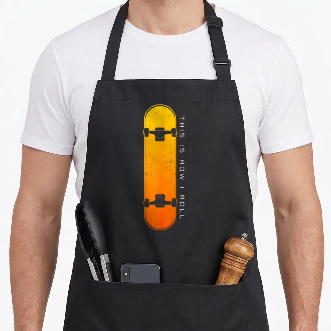 Skateboarding skateboard skateboarder apron - Yellow orange skateboard graphic with vertical white text THIS IS HOW I — shown on a black cotton canvas apron against a white background