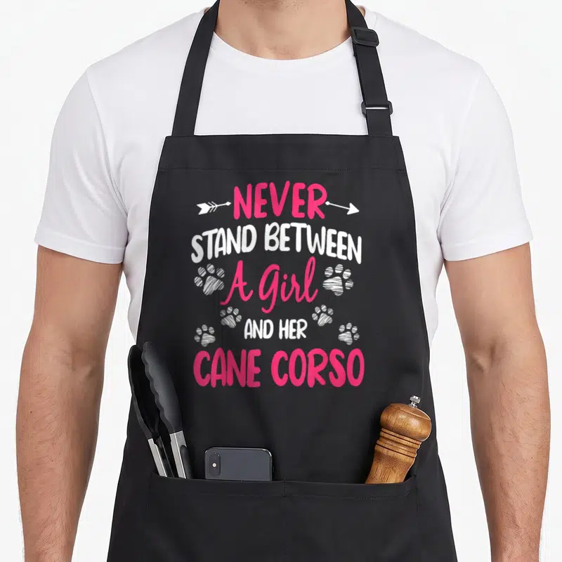 Stand cane apron - Pink and white text NEVER STAND BETWEEN A Girl AND HER CANE CORSO with arrows and paw prints — shown on a black cotton canvas apron against a white background
