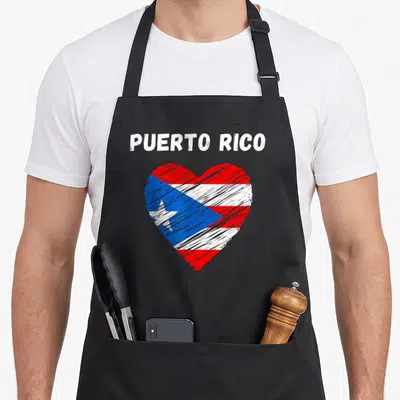 Puerto holiday apron - White text PUERTO RICO above a heart shape filled with red white and blue flag stripes and a star — shown on a black cotton canvas apron against a white background