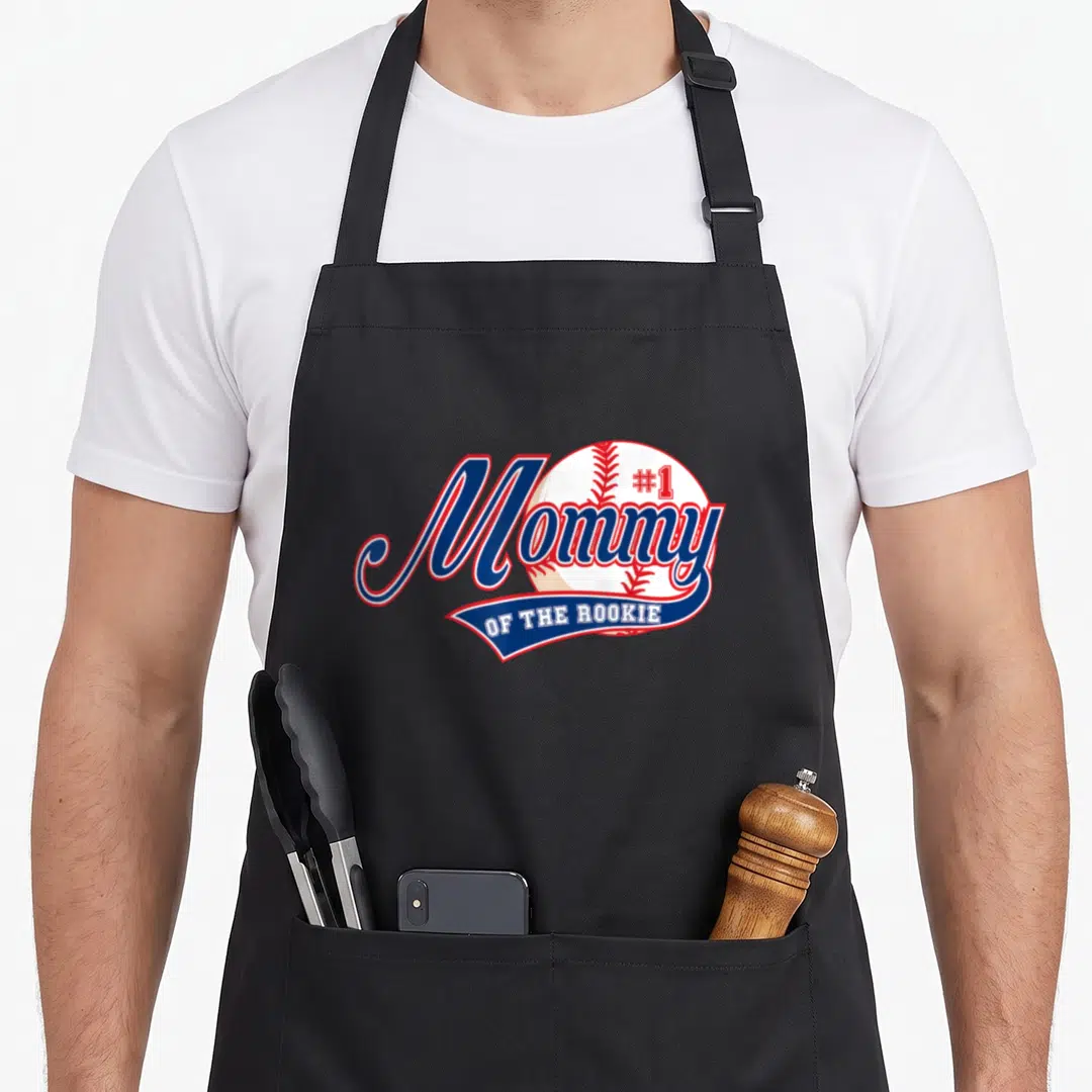 Rookie birthday apron - Mommy OF THE ROOKIE #1 baseball graphic in blue red white script — shown on a black cotton canvas apron against a white background