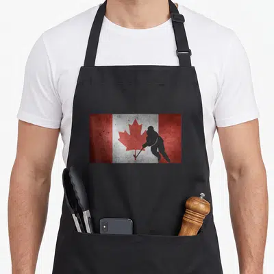 Hockey canadian aprons - Grey hockey player silhouette overlapping red maple leaf on distressed red and white flag — shown on a black cotton canvas apron against a white background