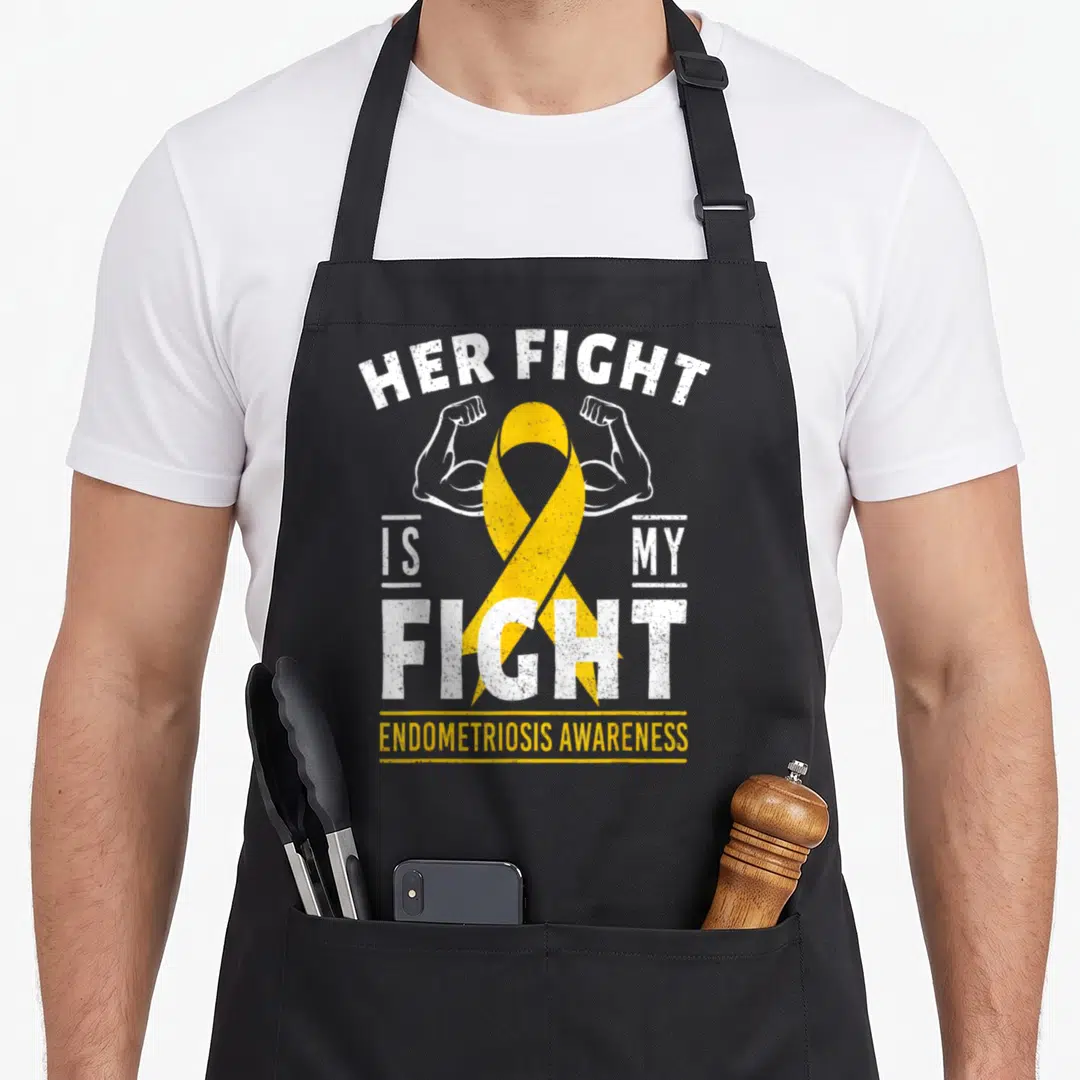 Fight endometriosis ribbon apron - Yellow ribbon flanked by flexed arms with Her Fight Is My Fight text — shown on a black cotton canvas apron against a white background