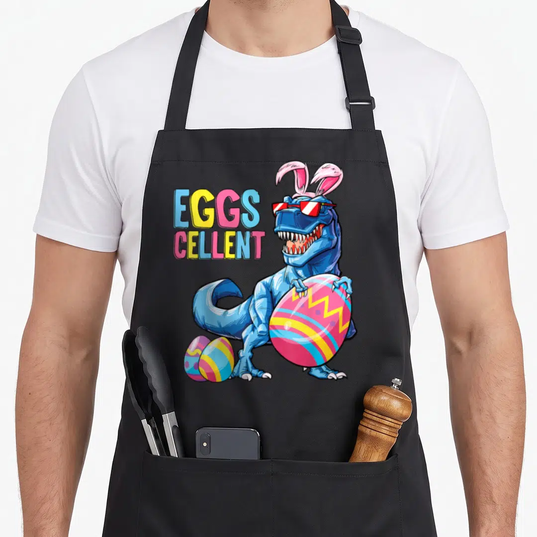 Rex easter egg apron - Blue dinosaur in bunny ears holding decorated egg next to text EGGS CELLENT — shown on a black cotton canvas apron against a white background
