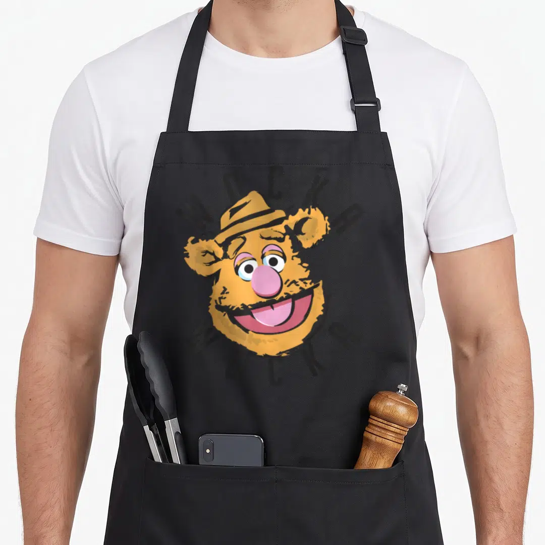 Wocka bear apron - Fozzie Bear head with arched WOCKA text in yellow and pink cartoon style — shown on a black cotton canvas apron against a white background