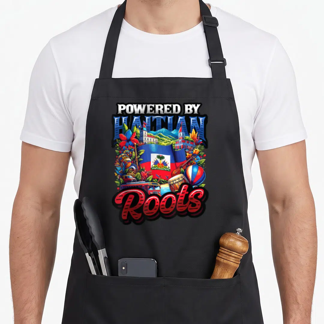 Powered haiti apron - POWERED BY HAITIAN Roots text with flag, drums, bus, and flowers in blue red yellow green — shown on a black cotton canvas apron against a white background