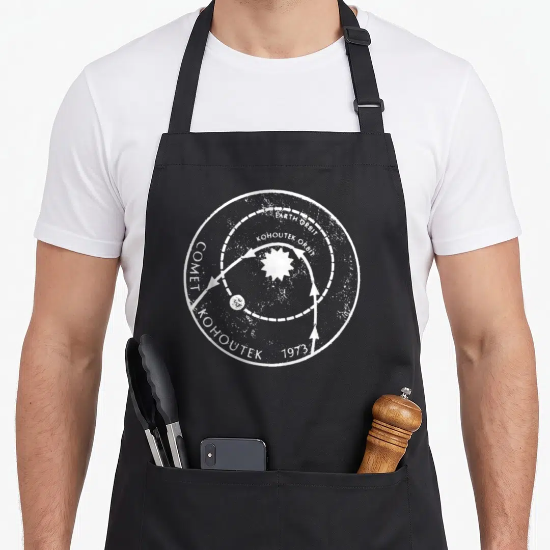 Comet science apron - Distressed white circular diagram showing Comet Kohoutek 1973 orbits around a central sun — shown on a black cotton canvas apron against a white background