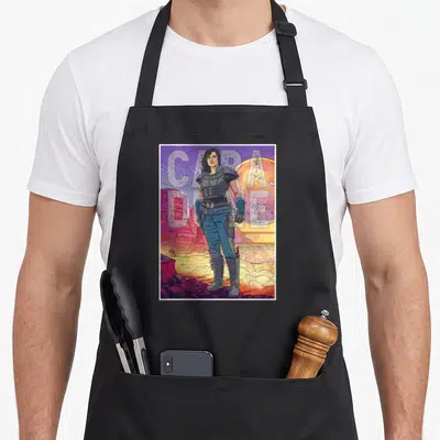 Cara great sand dunes apron - Cara Dune figure desert scene CAPA DUNE text planet purple orange blue red — shown on a black cotton canvas apron against a white background