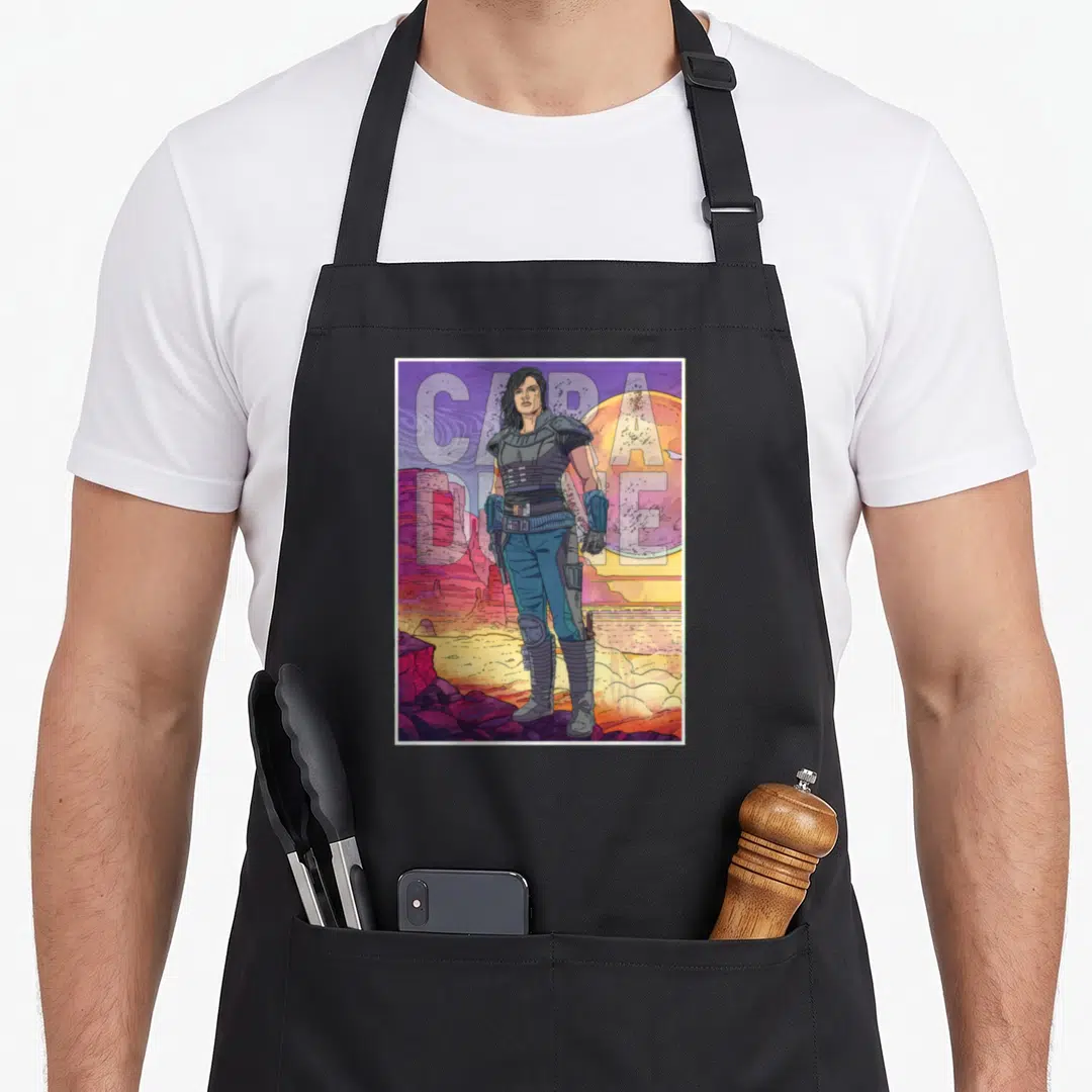 Cara great sand dunes apron - Cara Dune figure desert scene CAPA DUNE text planet purple orange blue red — shown on a black cotton canvas apron against a white background