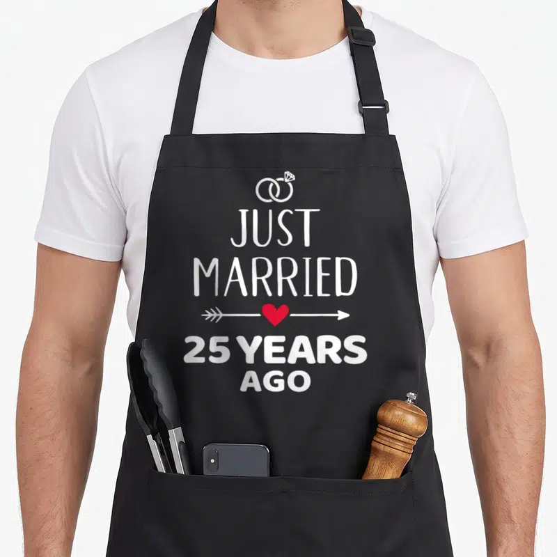 Married ago wedding apron - White rings and text Just Married 25 Years Ago with red heart arrow — shown on a black cotton canvas apron against a white background