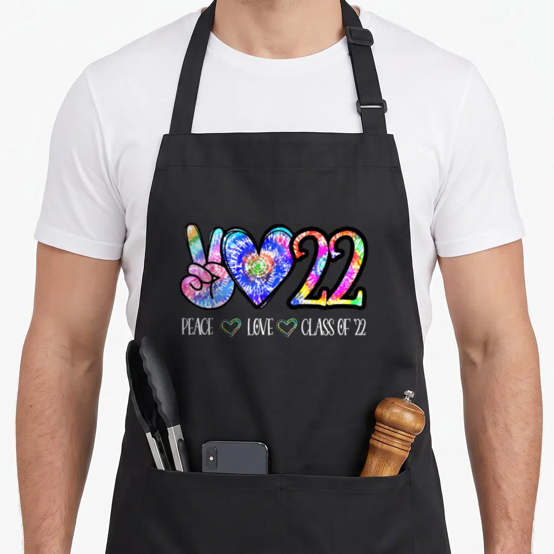Class tie-dye apron - Tie-dye peace sign heart and 22 graphic with white text reading PEACE LOVE CLASS OF 22 — shown on a black cotton canvas apron against a white background
