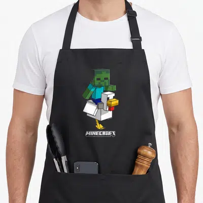 Jockey chicken apron - Blocky green zombie riding white chicken with MINECRAFT text below — shown on a black cotton canvas apron against a white background