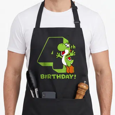 4th holiday apron - Green dinosaur standing in front of grey number 4 with BIRTHDAY text — shown on a black cotton canvas apron against a white background