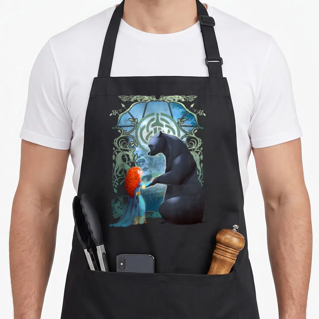 Brave bear apron - Black bear and red-haired girl in blue dress facing each other inside green ornamental frame — shown on a black cotton canvas apron against a white background