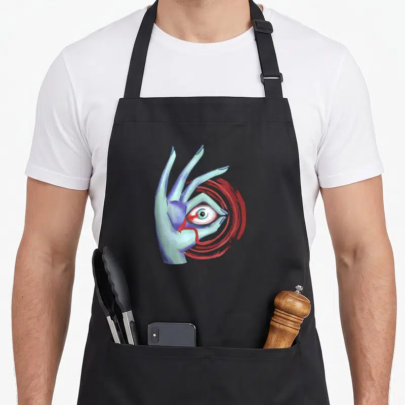 Weirdcore indie apron - Cartoon hand with embedded eye and red concentric circles on black fabric — shown on a black cotton canvas apron against a white background