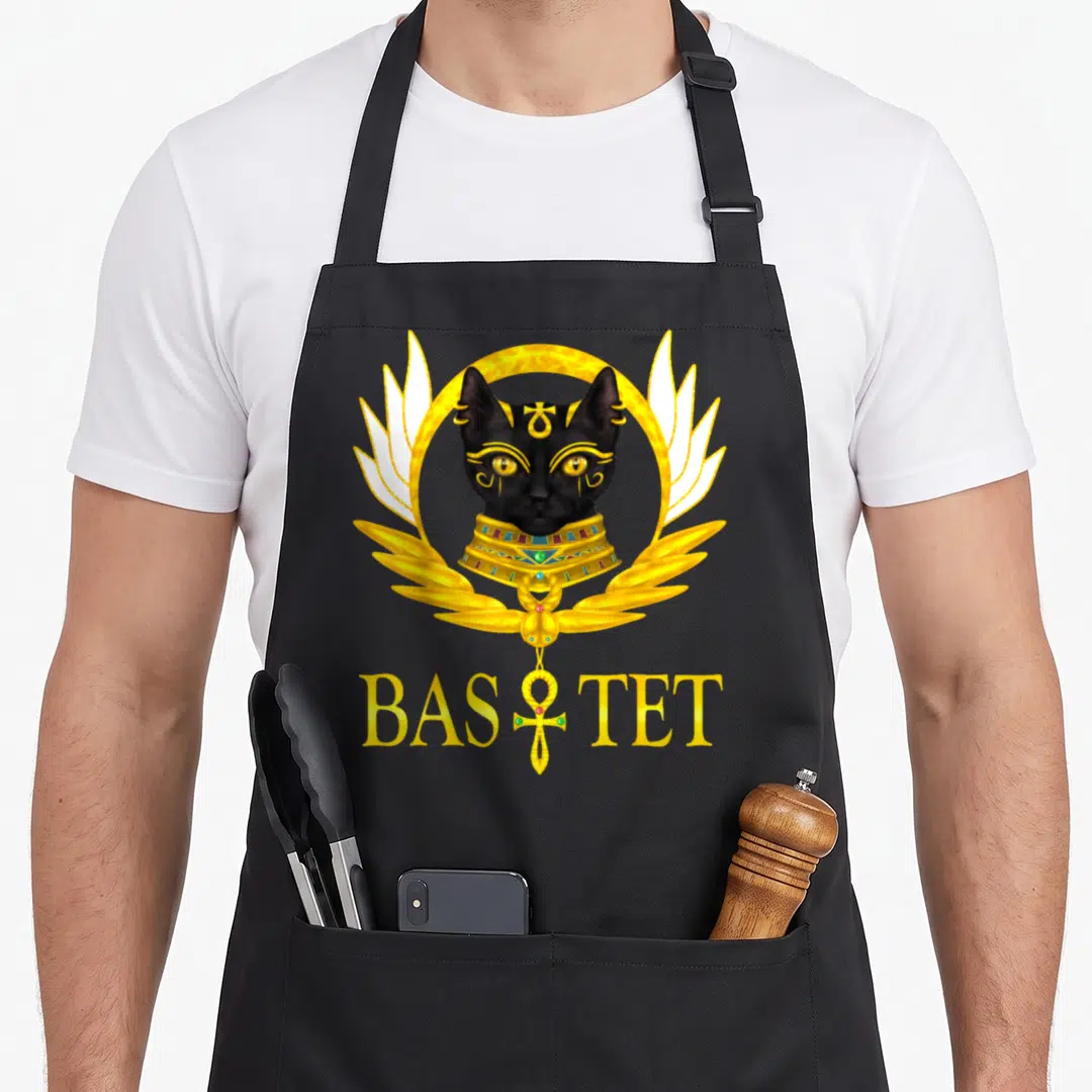 Goddess cat apron - Realistic black cat head in gold ring with wings and BASTET text — shown on a black cotton canvas apron against a white background