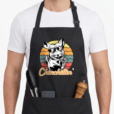 Chinchillin chinchilla dad apron - Cartoon chinchilla in sunglasses holding a drink against a retro striped sun — shown on a black cotton canvas apron against a white background