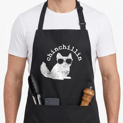Chinchilla chinchillin funny apron - White distressed chinchilla wearing sunglasses with arched chinchillin text above — shown on a black cotton canvas apron against a white background