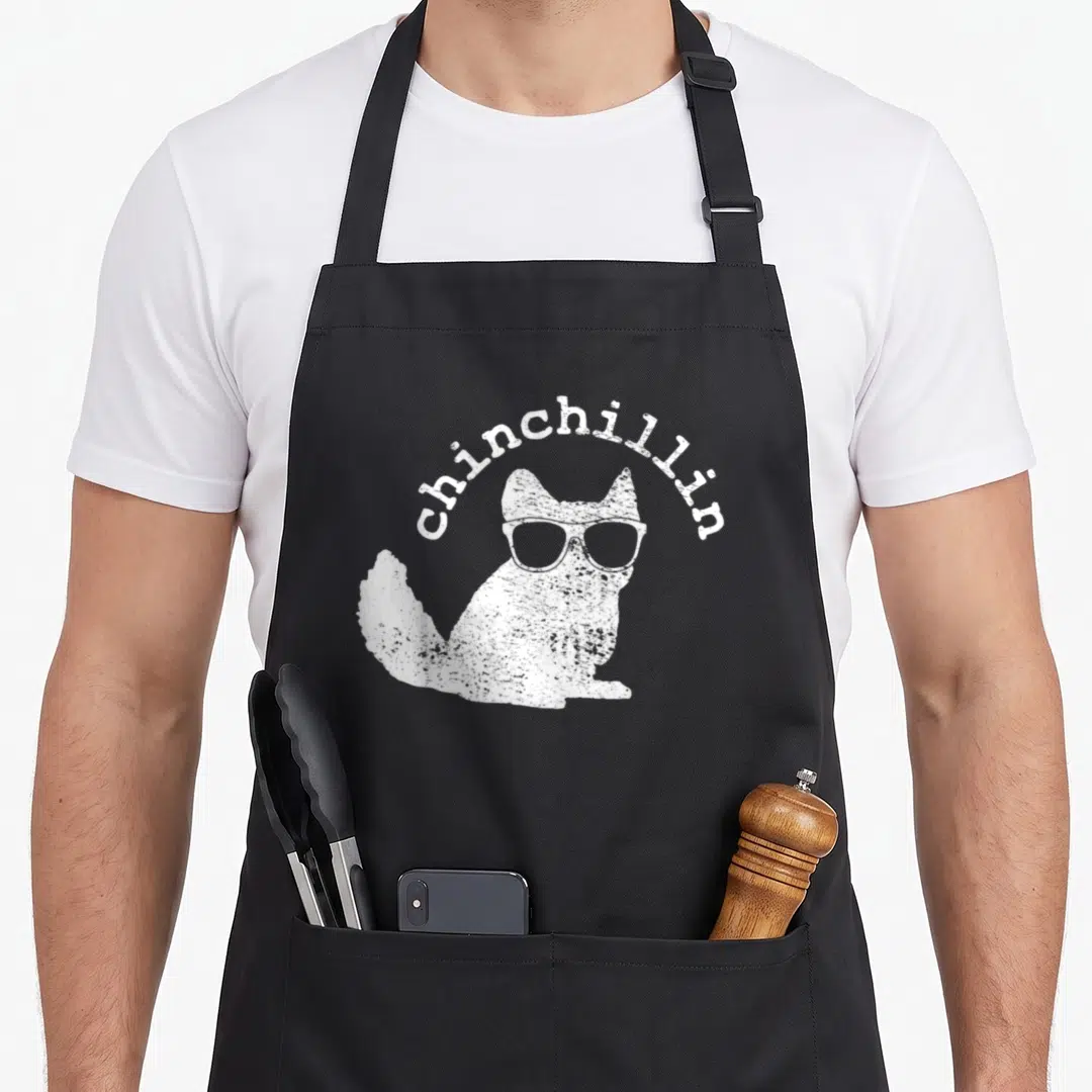 Chinchilla chinchillin funny apron - White distressed chinchilla wearing sunglasses with arched chinchillin text above — shown on a black cotton canvas apron against a white background
