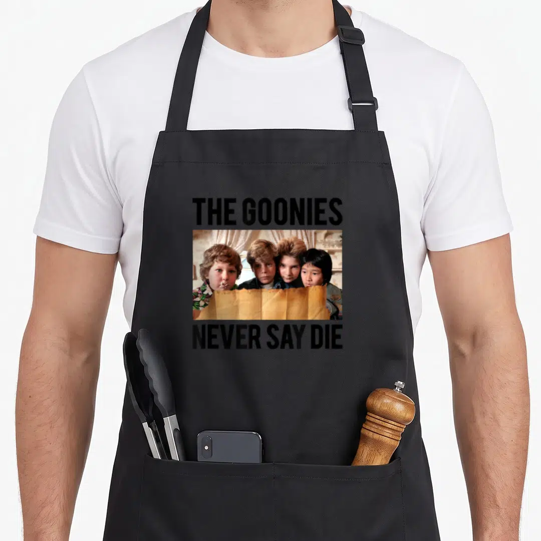 Die movie novelty apron - Four children looking over a map with text THE GOONIES and NEVER SAY DIE — shown on a black cotton canvas apron against a white background