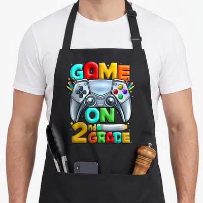 Game 2nd apron - Silver game controller surrounded by pencils and stars with colorful text — shown on a black cotton canvas apron against a white background
