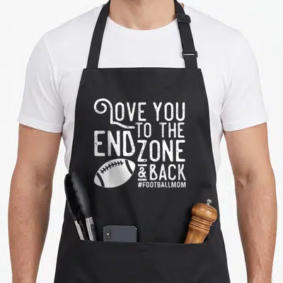 End football apron - White distressed text reading LOVE YOU TO THE END ZONE & BACK above a white football graphic — shown on a black cotton canvas apron against a white background