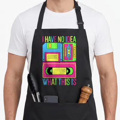 80s chef outfit with apron - I HAVE NO IDEA WHAT THIS IS text above three colorful retro tech items in neon pink yellow — shown on a black cotton canvas apron against a white background