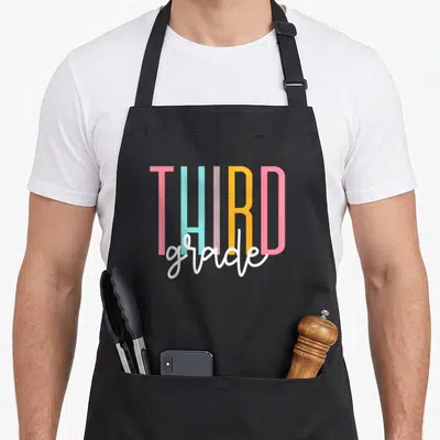 3rd squad teacher apron - THIRD grade text in pink light blue grey yellow white stacked typography — shown on a black cotton canvas apron against a white background