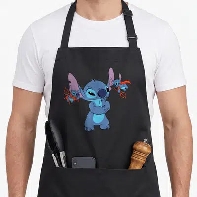 Novelty apron with pockets for women - Blue cartoon creature with two smaller devil figures holding red tridents — shown on a black cotton canvas apron against a white background