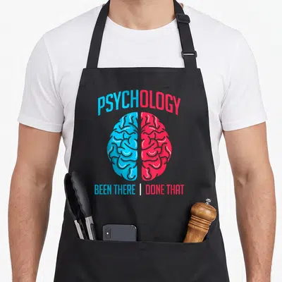 Brain student aprons - Split blue and red brain graphic with PSYCHOLOGY and BEEN THERE DONE THAT text — shown on a black cotton canvas apron against a white background