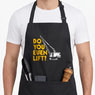 Geschenke construction apron - Yellow stacked text DO YOU EVEN LIFT next to a white crane with hanging hook — shown on a black cotton canvas apron against a white background