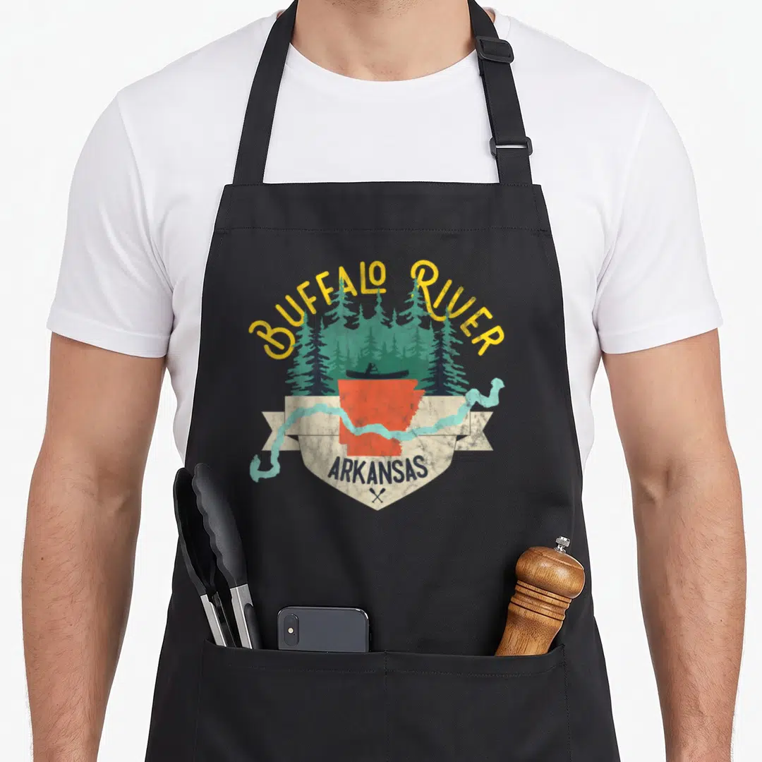 River buffalo apron - Retro shield with red Arkansas map, kayaker, yellow text, and light blue river on beige ribbon — shown on a black cotton canvas apron against a white background